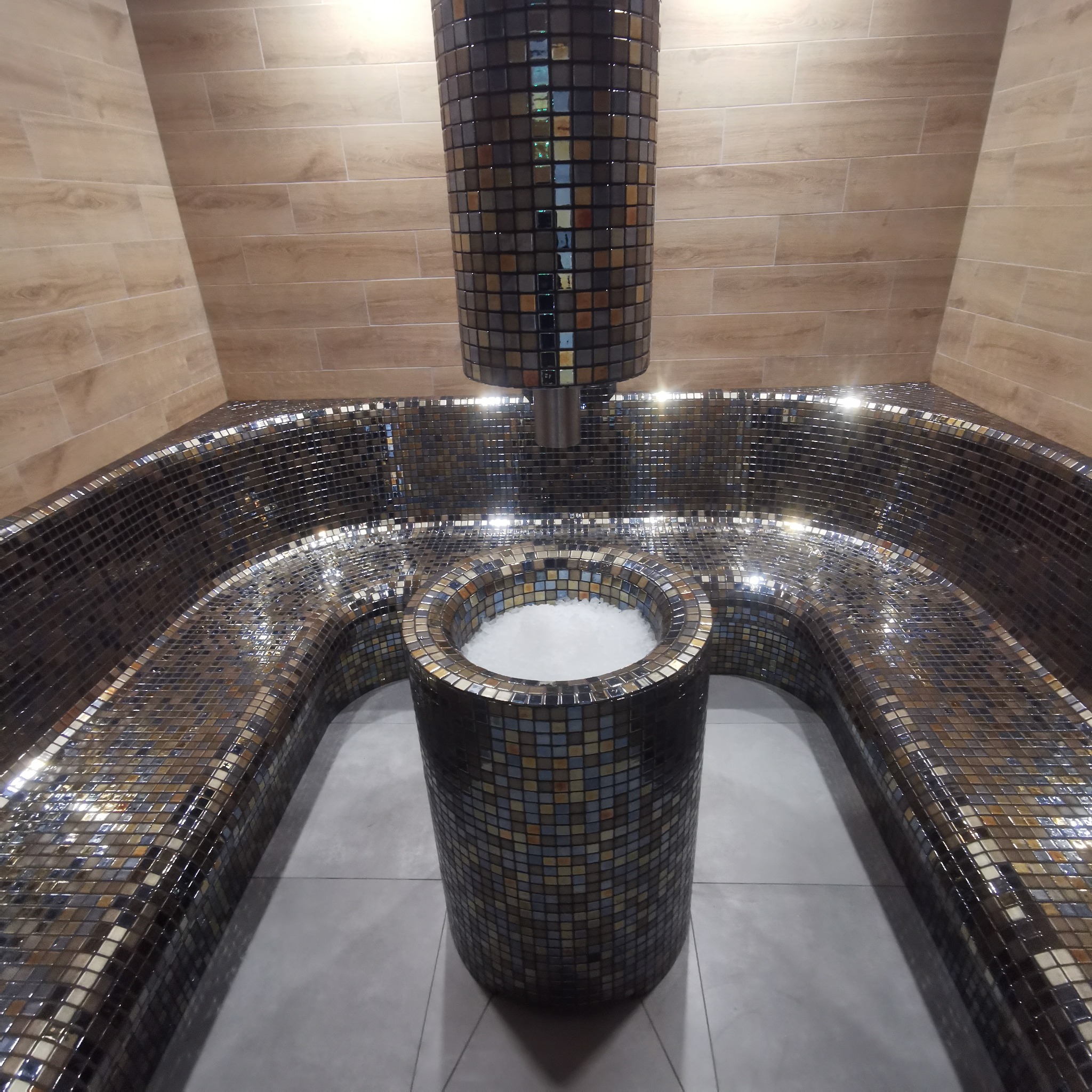 Mozaikowa kabina lodowa z siedziskami wyłożonymi błyszczącą mozaiką, z pojemnikiem na lód i instalacją podającą lód, wykończona jasnymi płytkami imitującymi drewno.