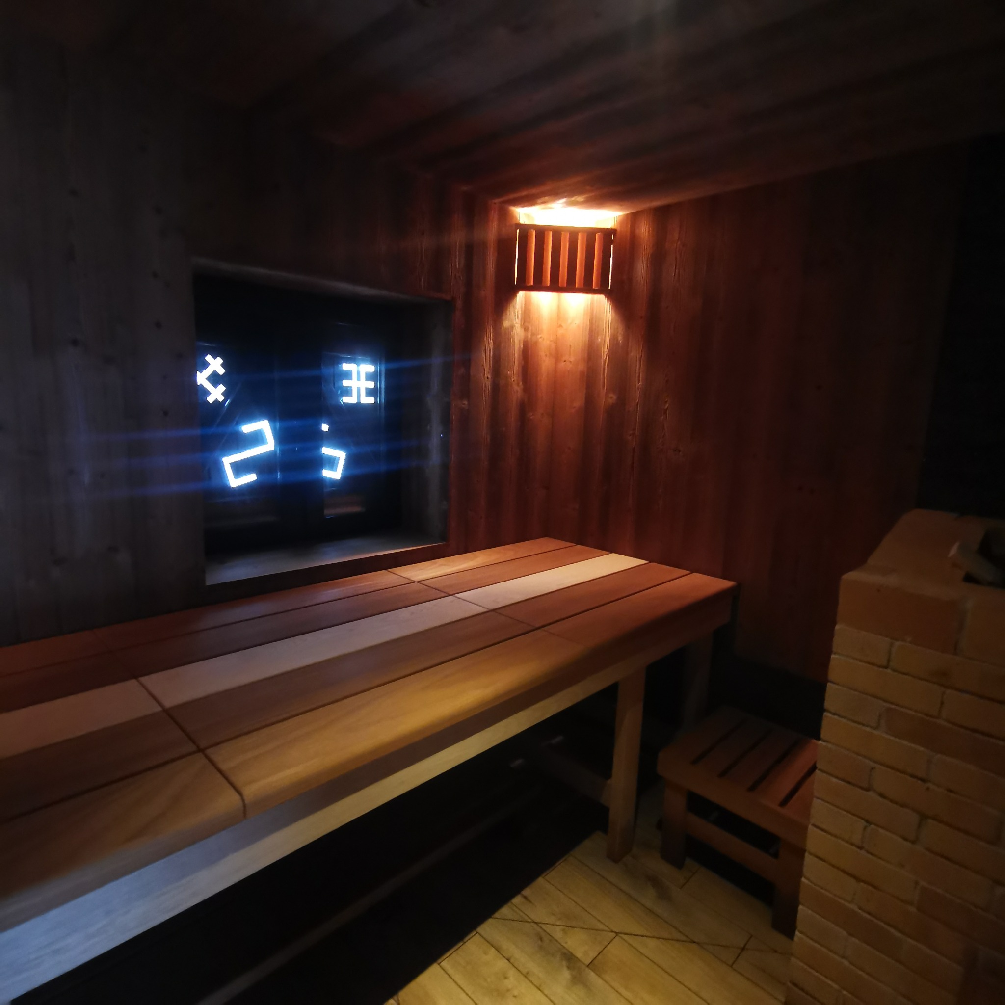 Wnętrze sauny z drewnianymi ławami o zróżnicowanej kolorystyce, oświetleniem punktowym i cyfrowym wyświetlaczem temperatury w tle.