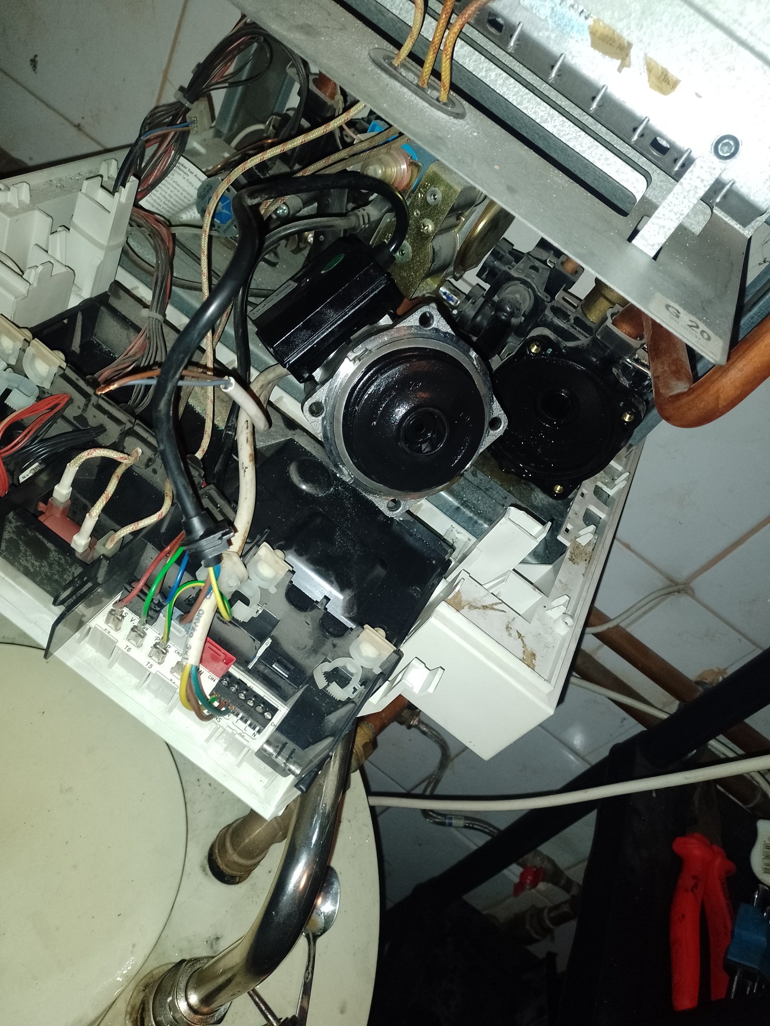 Otwarty piec gazowy w trakcie naprawy, widoczne przewody, elementy elektroniczne i hydrauliczne, z bliska, z narzędziami w tle.