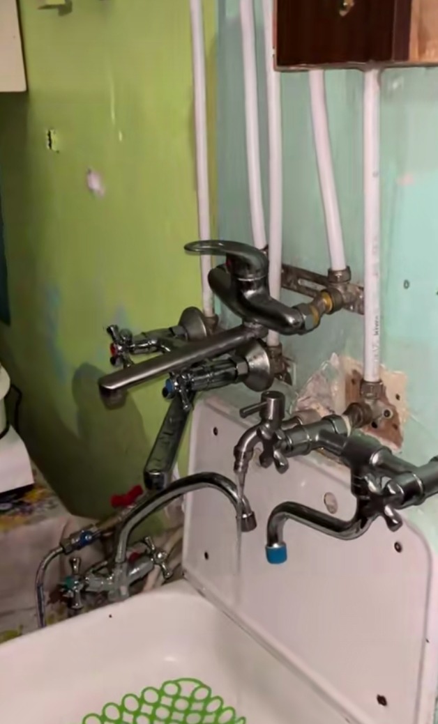 Złożony układ hydrauliczny z wieloma kranami i rurami zamontowanymi na ścianie w łazience o nierównych ścianach.