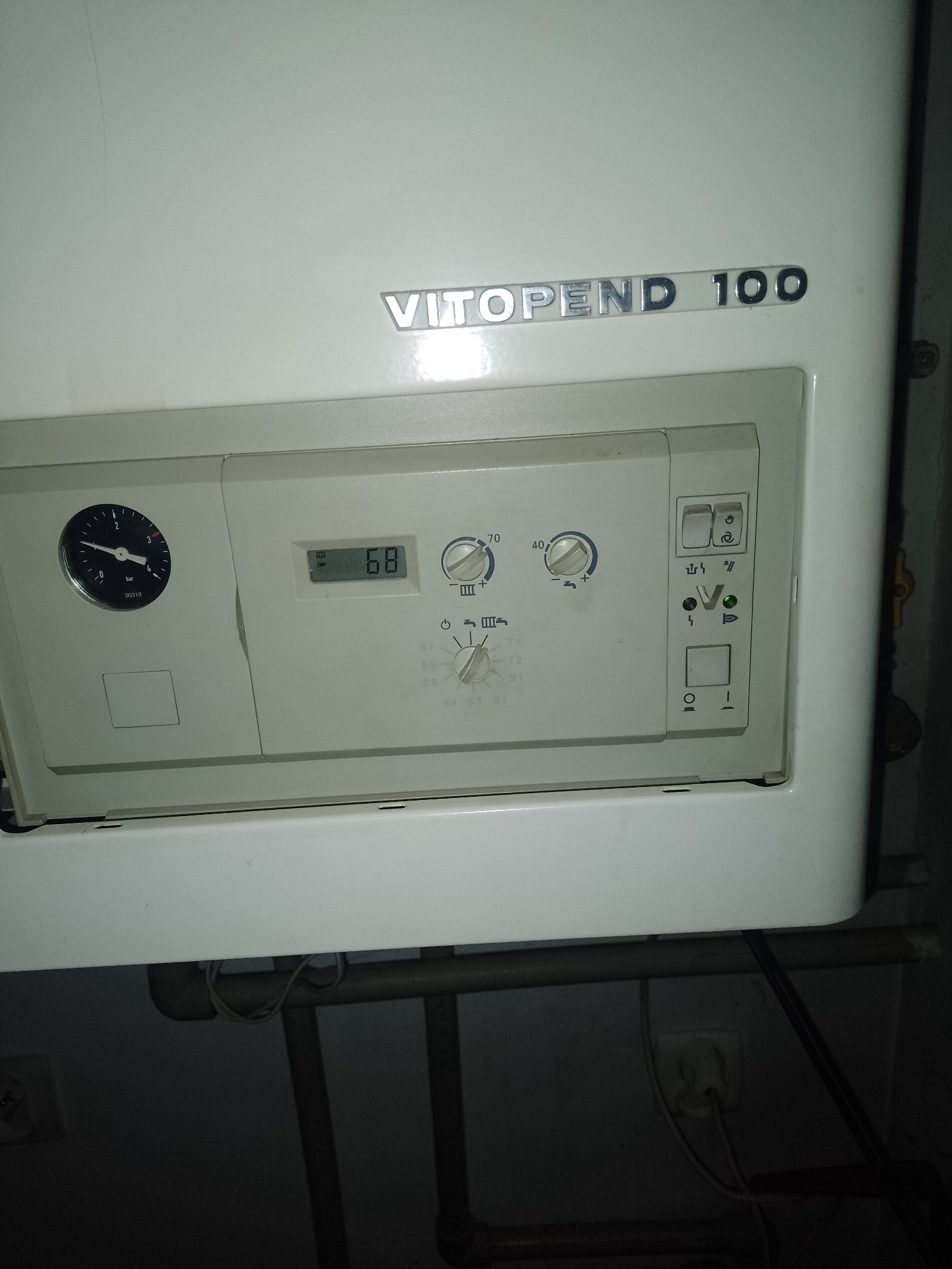 Biały piec gazowy Viessmann Vitopend 100 z widocznym panelem sterowania, manometrem wskazującym niskie ciśnienie, wyświetlaczem temperatury 68 stopni, pokrętłami regulacji i zieloną diodą...