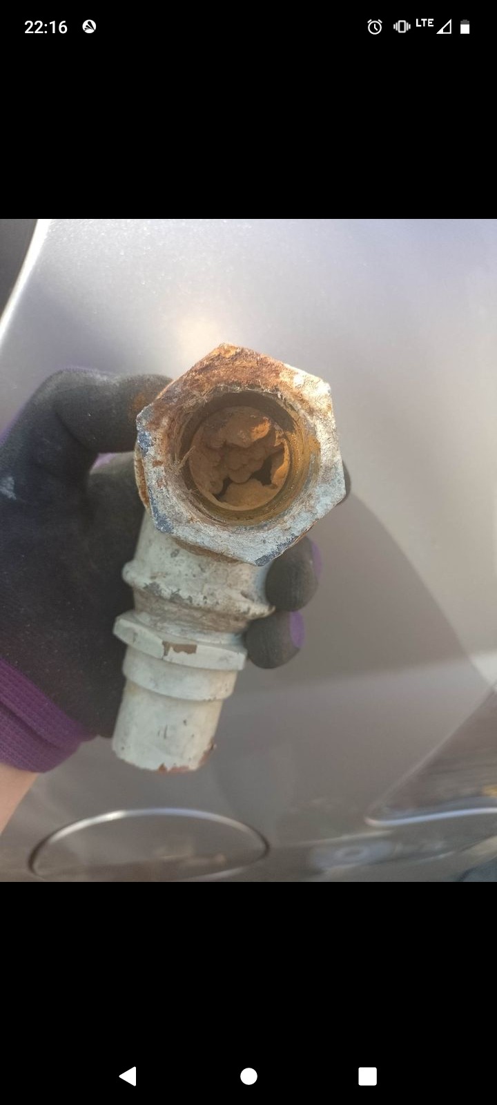 Zardzewiała złączka hydrauliczna, trzymana w rękawicy roboczej, widoczne osady wewnątrz.