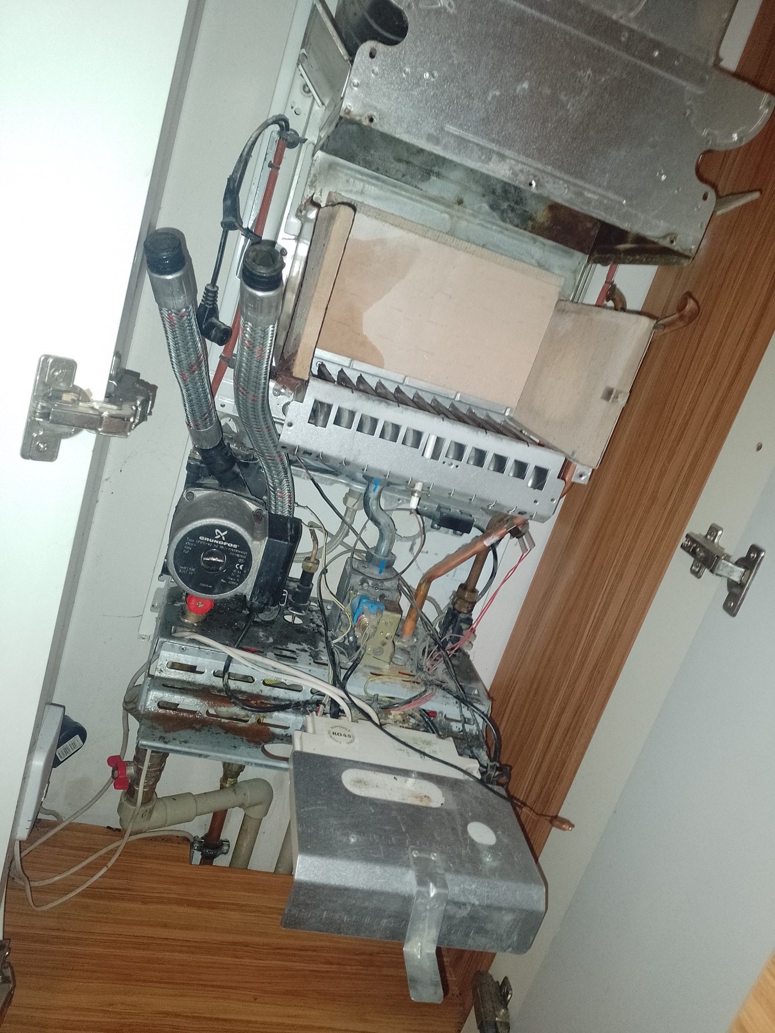 Otwarty piec gazowy w zabudowie, widoczne elementy instalacji, w tym pompa obiegowa Grundfos i liczne przewody.