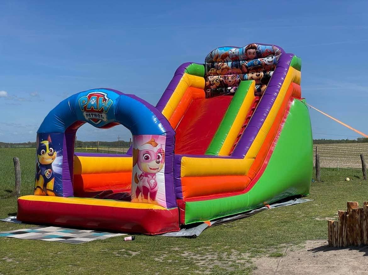 Kolorowa dmuchana zjeżdżalnia z motywem bajki Psi Patrol, ustawiona na trawie w słoneczny dzień.