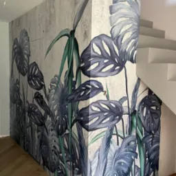 Wnętrze z fototapetą przedstawiającą motyw roślinny monstery na ścianie przy schodach, widoczny fragment podłogi z parkietu ułożonego w jodełkę.