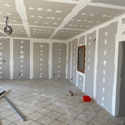 RENONEUF - Wnętrze w trakcie prac wykończeniowych: ściany i sufit pokryte płytami gipsowo-kartonowymi, widoczne łączenia i szpachlowane miejsca po wkrętach, elementy instalacji elektrycznej.