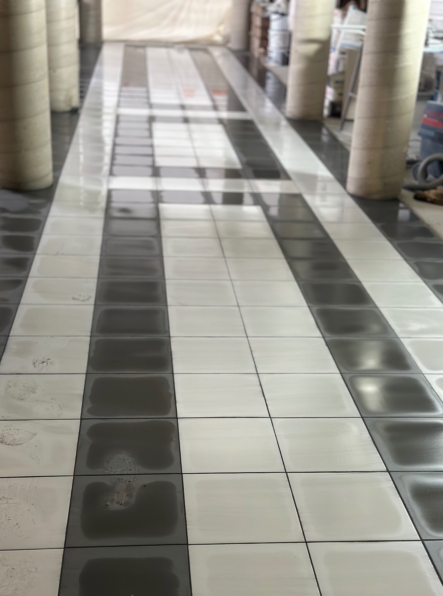 Ułożona podłoga z płytek w szachownicę (szary i biały) wzdłuż kolumn. Widok z dołu, perspektywa zbieżna. Płytki mokre, odbijają światło.