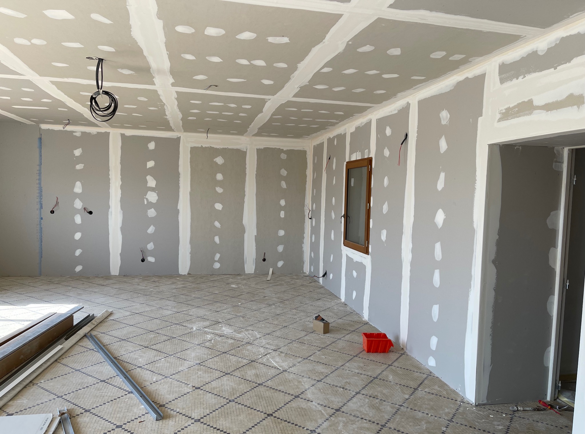 Wnętrze w trakcie prac wykończeniowych: ściany i sufit pokryte płytami gipsowo-kartonowymi, widoczne łączenia i szpachlowane miejsca po wkrętach, elementy instalacji elektrycznej.