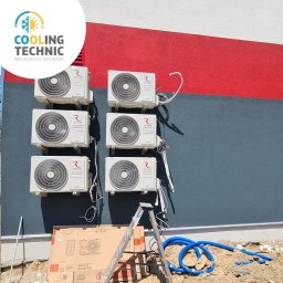 Cooling Technic Wojciech Niciecki - Sześć klimatyzatorów zamontowanych na ścianie budynku z czerwoną i szarą farbą, widoczna drabina, kartony i niebieskie rury instalacyjne.