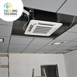Cooling Technic Wojciech Niciecki - Kasetonowa klimatyzacja sufitowa w biurze, widoczne instalacje i przewody, w tle drabina malarska, instalacja w trakcie prac wykończeniowych.