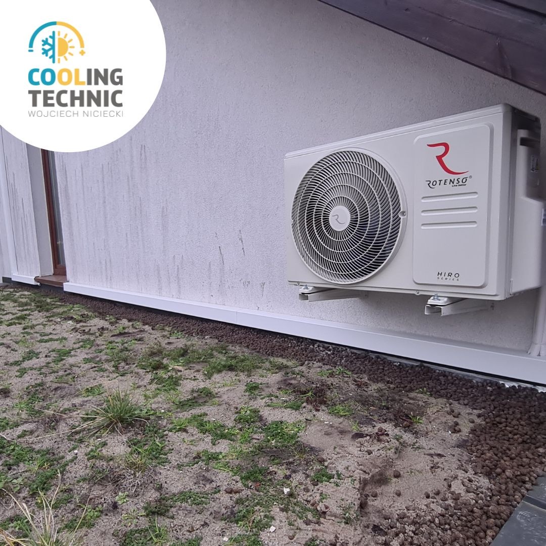 Zewnętrzna jednostka klimatyzacji Rotenso Hiro zamontowana na białej ścianie domu, widoczny fragment ogrodu z ziemią i kamieniami, logo firmy Cooling Technic w lewym górnym rogu.