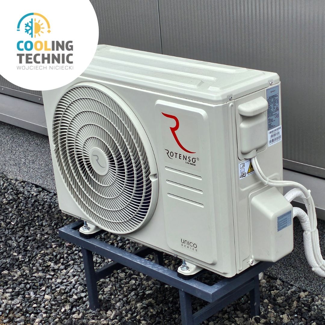 Zewnętrzna jednostka klimatyzacji Rotenso Unico Series na metalowym stelażu, umieszczona na żwirowym podłożu przy metalowej ścianie budynku.