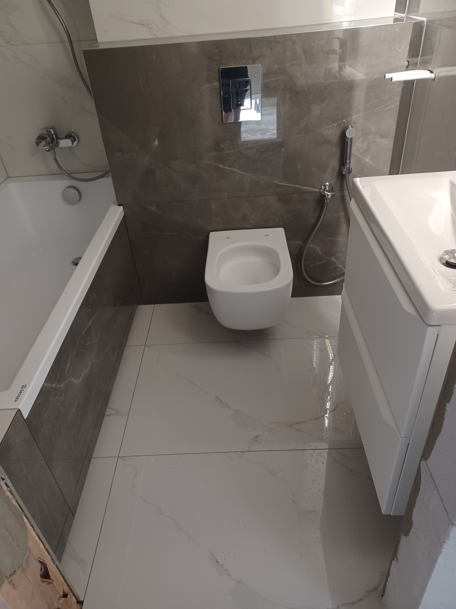 Nowoczesna łazienka po remoncie: marmurowe płytki, podwieszana toaleta, biała umywalka z szafką, chromowana armatura. Widok z dołu, podkreślający przestronność.