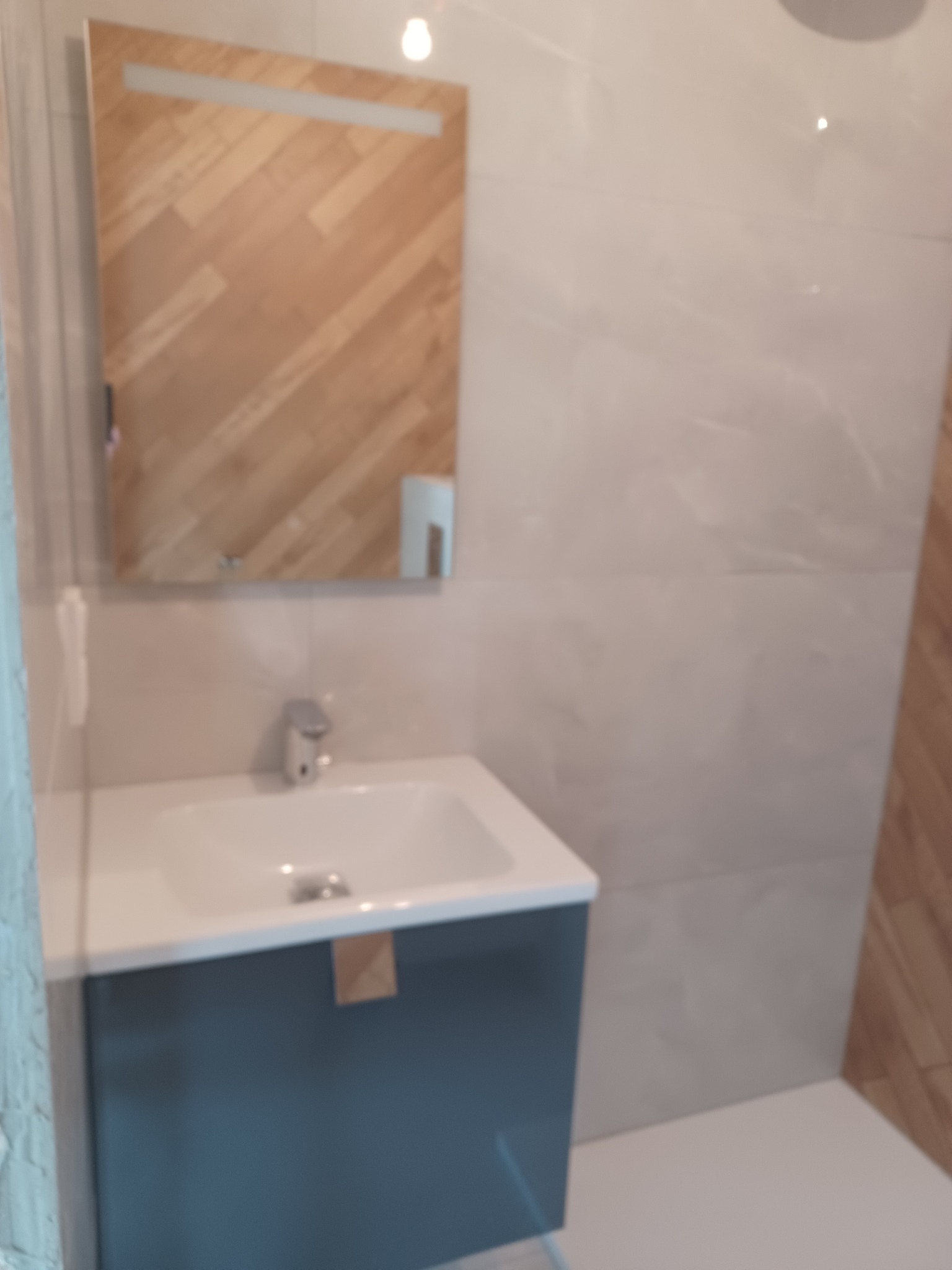 Wykończona łazienka: umywalka z szafką w odcieniach szarości, lustro z drewnianym wzorem i płytki imitujące marmur. Nowoczesny design.