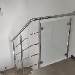 Spawstal-balustrady nierdzewne - Schody z balustradą ze stali nierdzewnej i szkła, widok z góry na stopnie wyłożone płytkami, na ścianie lampa w stylu industrialnym.