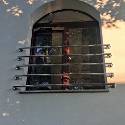 Spawstal-balustrady nierdzewne - Nierdzewna balustrada okienna z czterema poziomymi prętami i zaokrąglonymi zakończeniami, zamontowana na elewacji budynku z oknem łukowym.