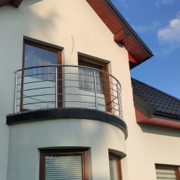 Spawstal-balustrady nierdzewne - Biały dom z balkonem zabezpieczonym nowoczesną, metalową balustradą z poziomych rurek, na tle błękitnego nieba z chmurami.