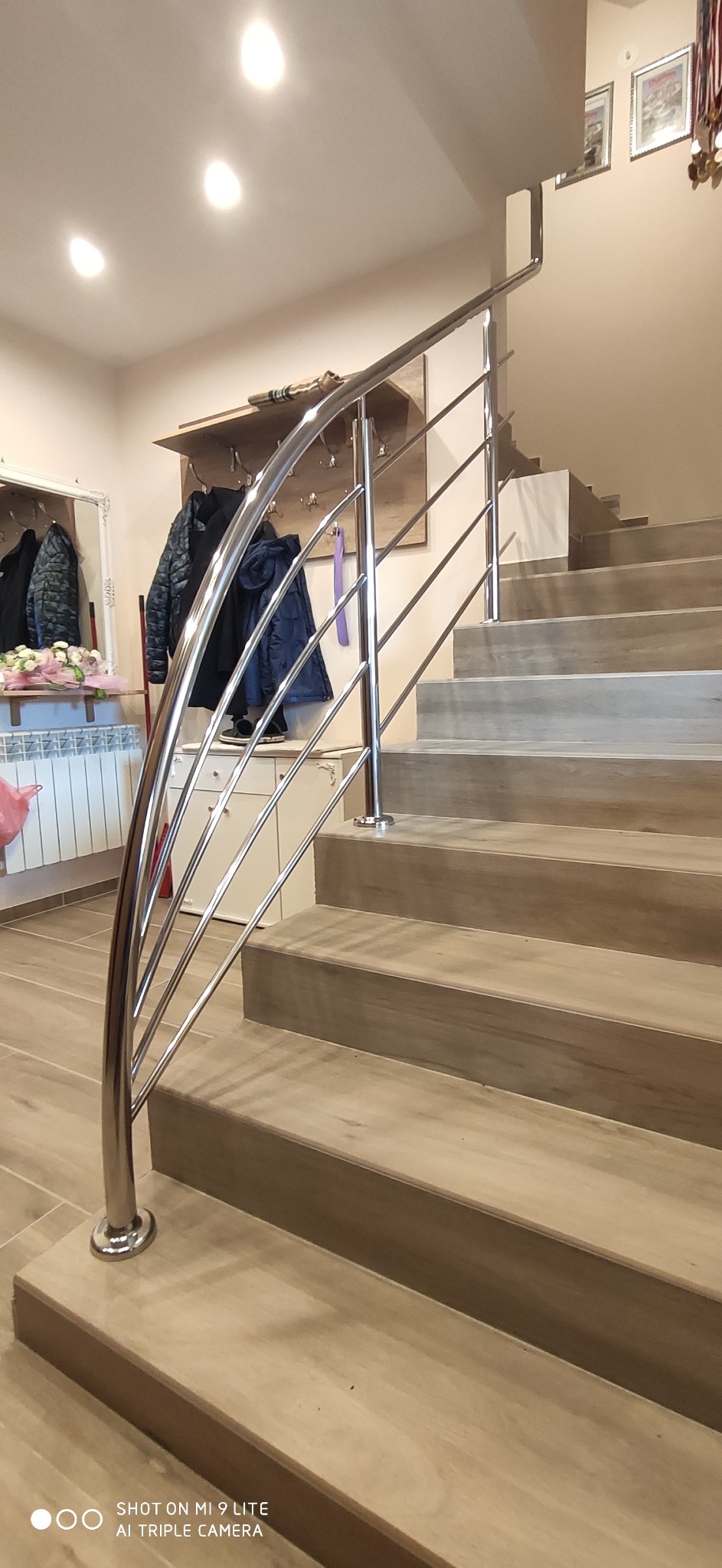 Nowoczesne schody z drewnopodobnymi stopniami i błyszczącą, metalową balustradą z poziomymi prętami, widok z dołu.