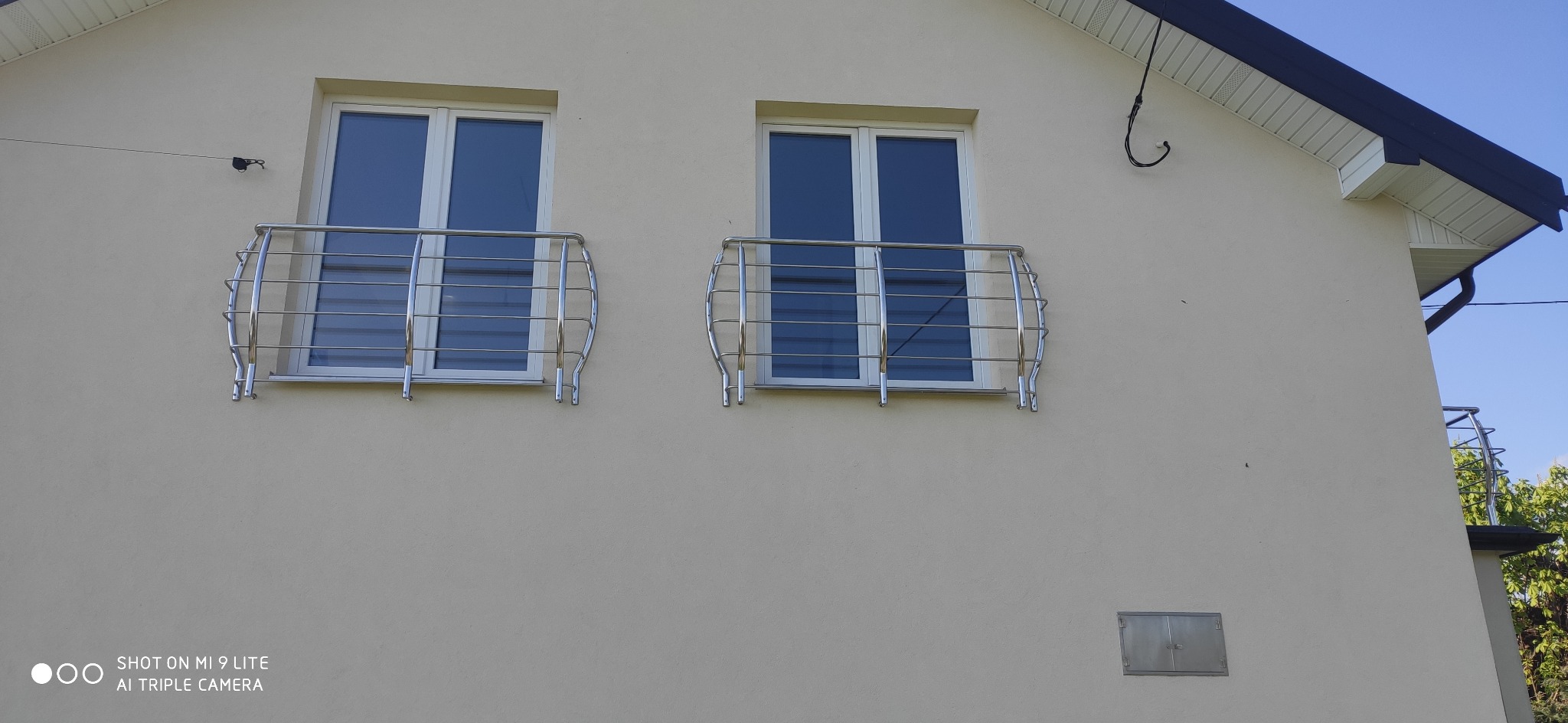 Dwa okna na elewacji budynku z zamontowanymi zewnętrznymi, metalowymi zabezpieczeniami okiennymi w formie balustrady z poziomymi prętami.