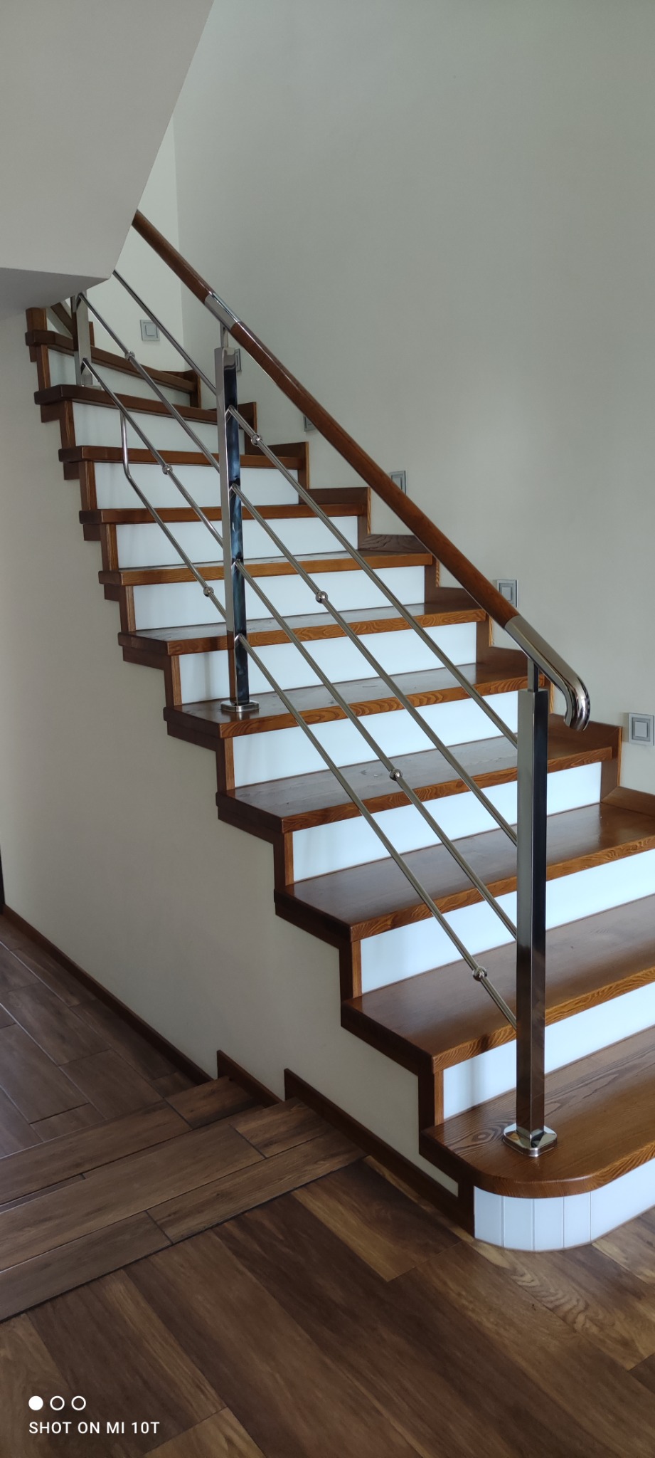 Schody drewniane z białymi podstopnicami i balustradą ze stali nierdzewnej, drewniany pochwyt, widok z dołu na kilka stopni.