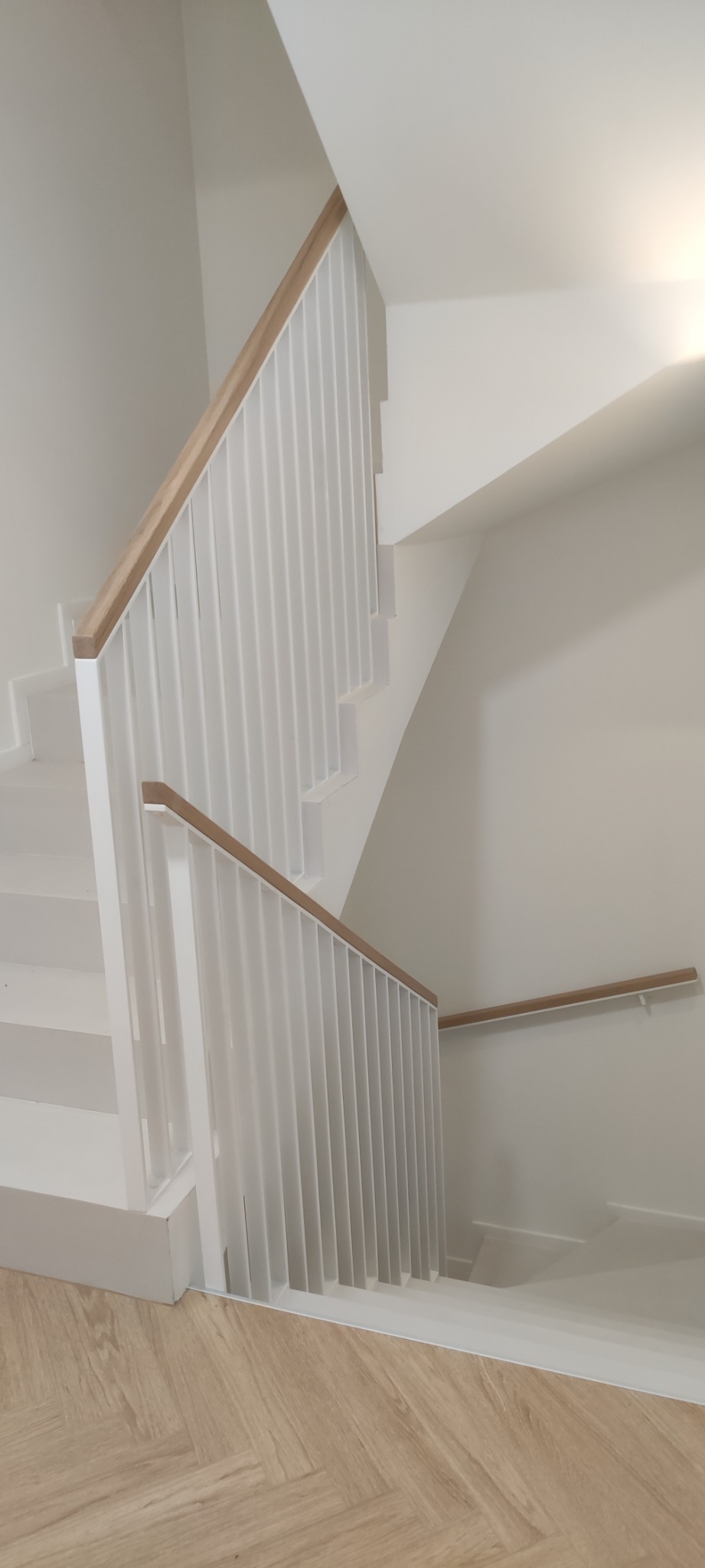 Klatka schodowa z białymi schodami i białą balustradą z drewnianym pochwytem w domu w Nieborowie, widok z góry na dół.