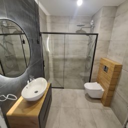 Dom-tech - Nowoczesna łazienka z szarymi płytkami, kabiną prysznicową z czarną ramą, umywalką nablatową na drewnianej szafce i podwieszaną toaletą z drewnianą zabudową.