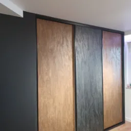 Nowoczesna szafa wnękowa z przesuwnymi drzwiami o teksturze drewna i kamienia, wkomponowana w ciemną ścianę, widok z dołu.