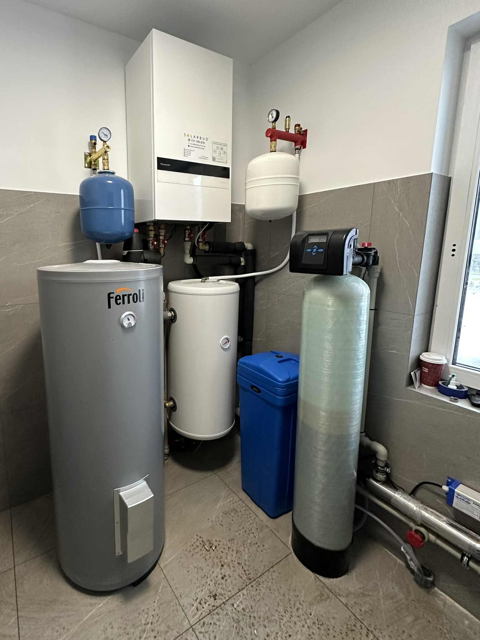 Kompletna instalacja grzewcza z pompą ciepła Solarbud, zbiornikami Ferroli i filtrem wody w kotłowni wykończonej płytkami imitującymi kamień.