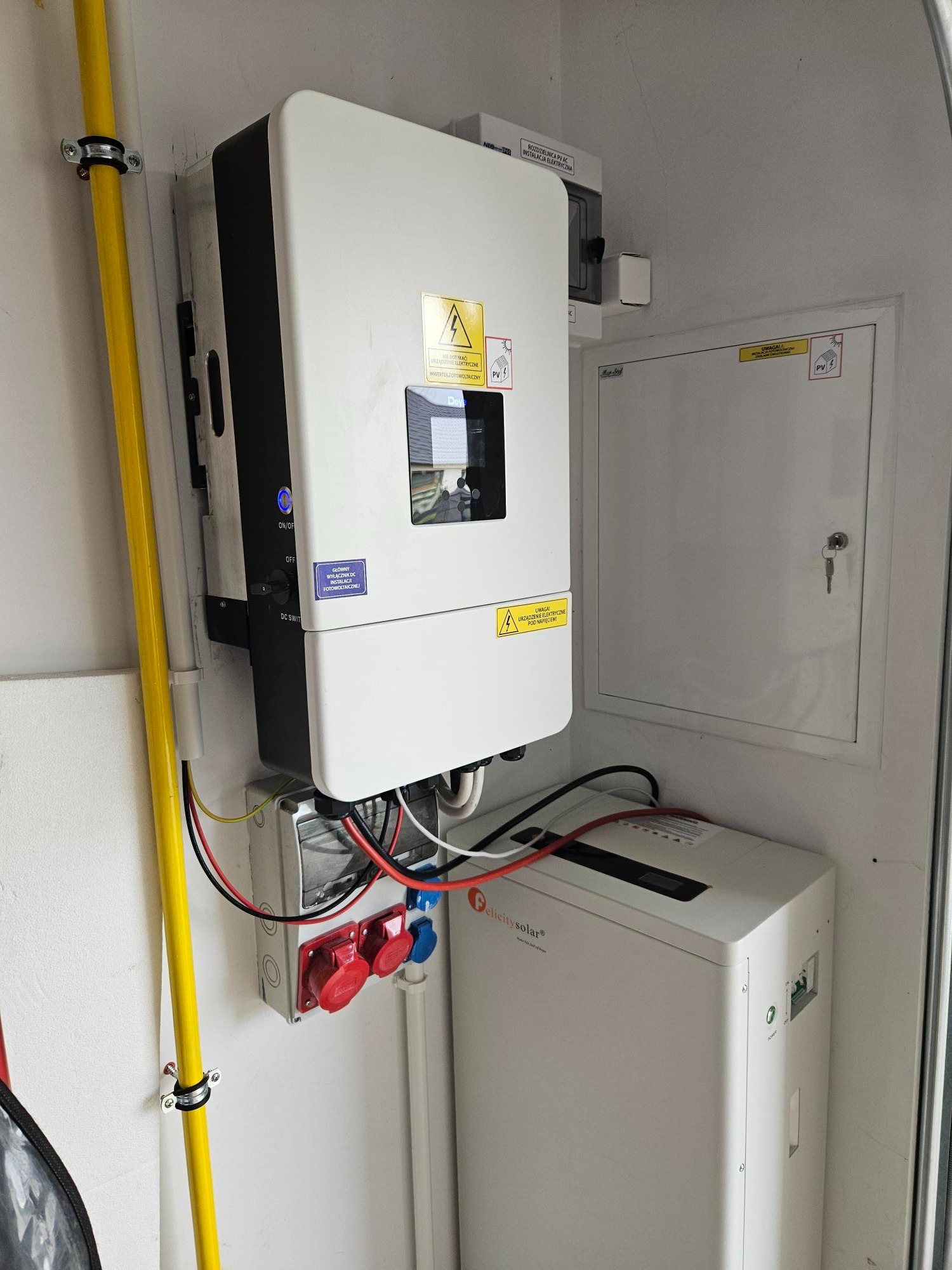 Kompletna instalacja fotowoltaiczna w pomieszczeniu: inwerter, magazyn energii Felicity Solar, rozdzielnica i okablowanie. Żółta rura gazowa w tle.