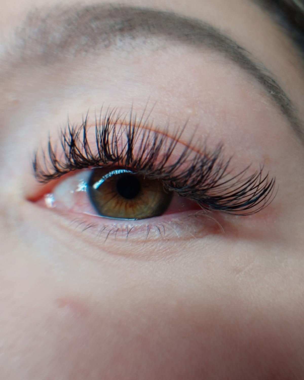 Zbliżenie na oko z brązową tęczówką i przedłużonymi, gęstymi, czarnymi rzęsami; widoczny delikatny blask w oku.
