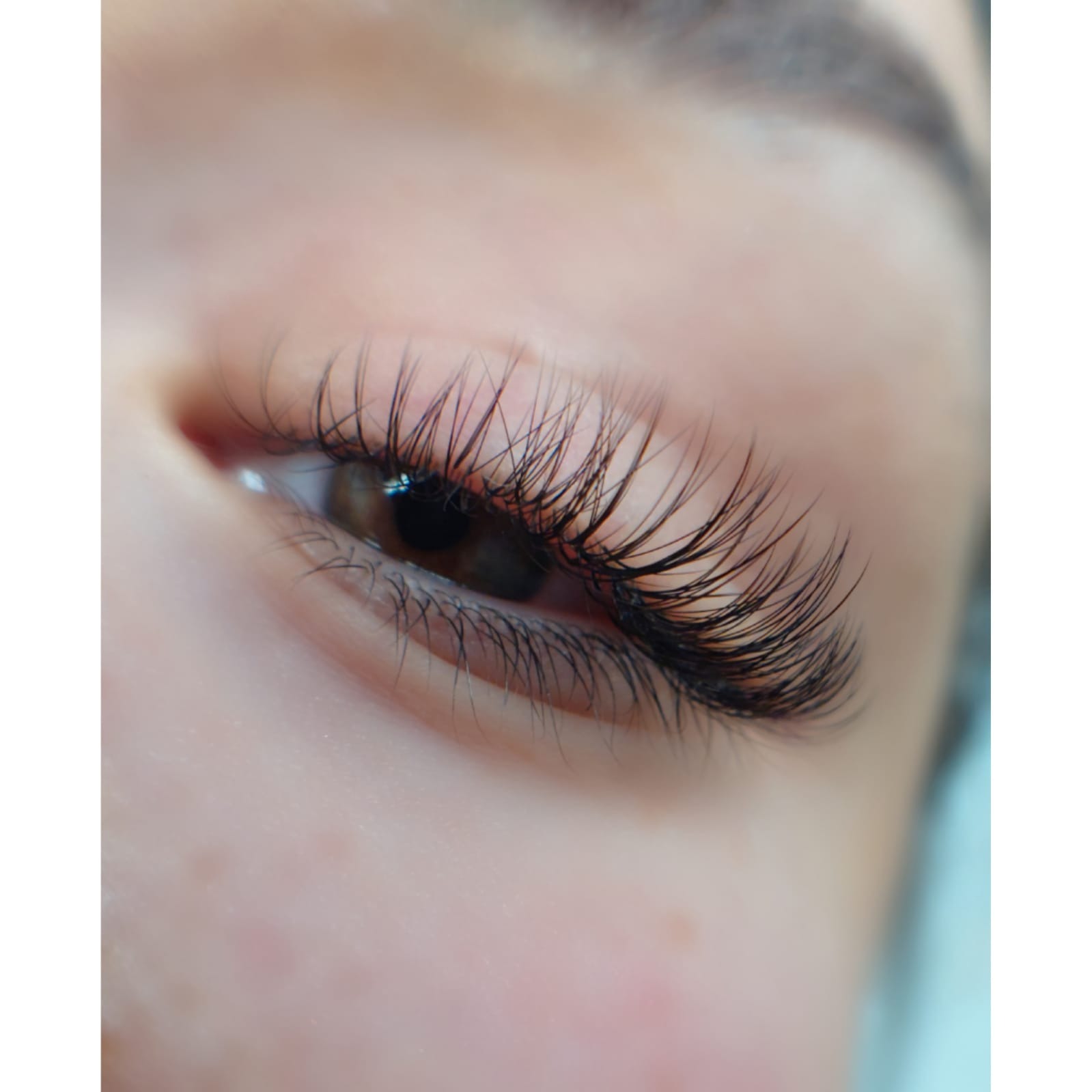 Zbliżenie na oko z długimi, gęstymi, profesjonalnie przedłużonymi rzęsami, widoczne brązowe tęczówki i delikatne włoski na dolnej powiece.