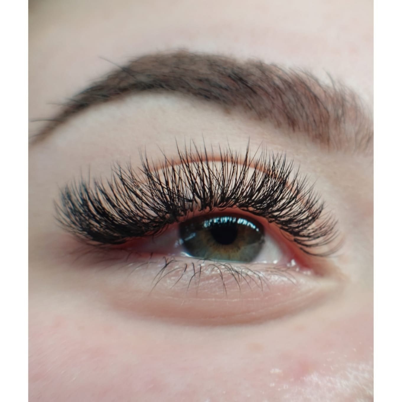Zbliżenie na oko z gęstymi, profesjonalnie przedłużonymi czarnymi rzęsami, widoczna brązowa tęczówka i naturalna brew.