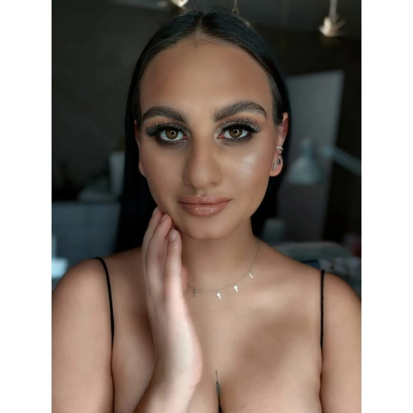 Portret kobiety z wieczorowym makijażem: podkreślone oczy z brokatem, błyszcząca cera, pełne usta w odcieniu nude, delikatna biżuteria.