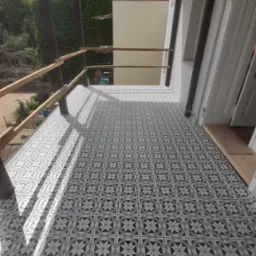 Wyłożony wzorzystymi, szaro-białymi płytkami balkon z drewnianą balustradą, widok z góry, cień rzucany przez konstrukcję dachu.