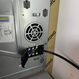 EIM - Paweł Mróz - Widok z tyłu płyty indukcyjnej z podłączonym kablem zasilającym do listwy zaciskowej; widoczne przewody: niebieski, brązowy, żółto-zielony.