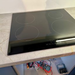 EIM - Paweł Mróz - Czarna płyta indukcyjna czteropalnikowa wbudowana w blat o wzorze marmuru, widoczne narzędzia elektryczne pod spodem.