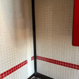 Fragment kuchni z białymi mozaikowymi płytkami z czerwonym paskiem, czarną ramą okapu i widoczną częścią kuchenki gazowej.