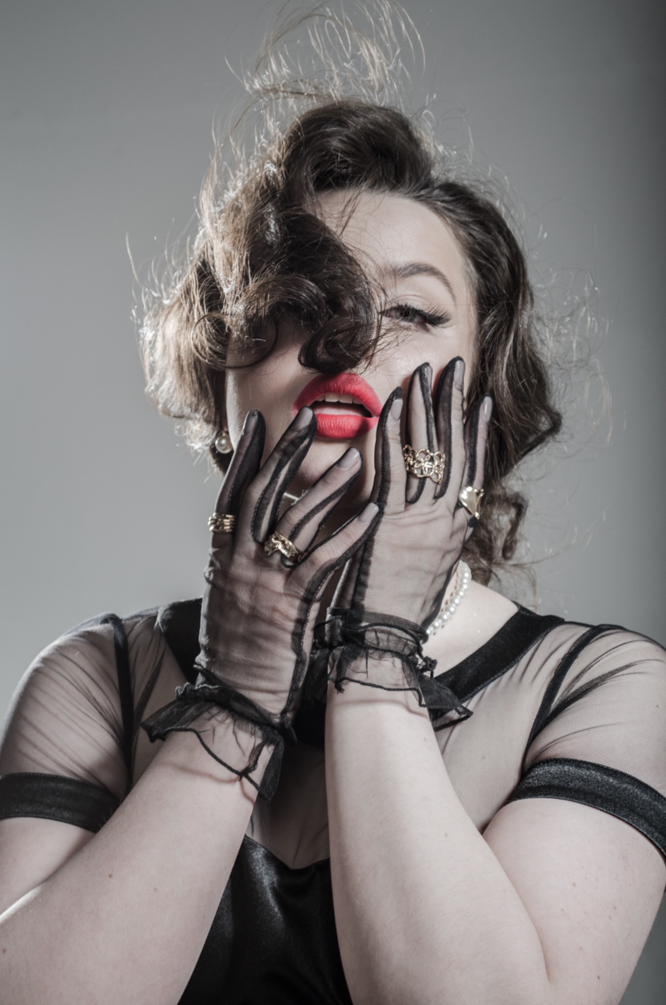 Portret kobiety w stylu retro z czerwonymi ustami, w czarnej, prześwitującej bluzce, perłach i tiulowych rękawiczkach z pierścionkami, wykonany w studiu w Warszawie.