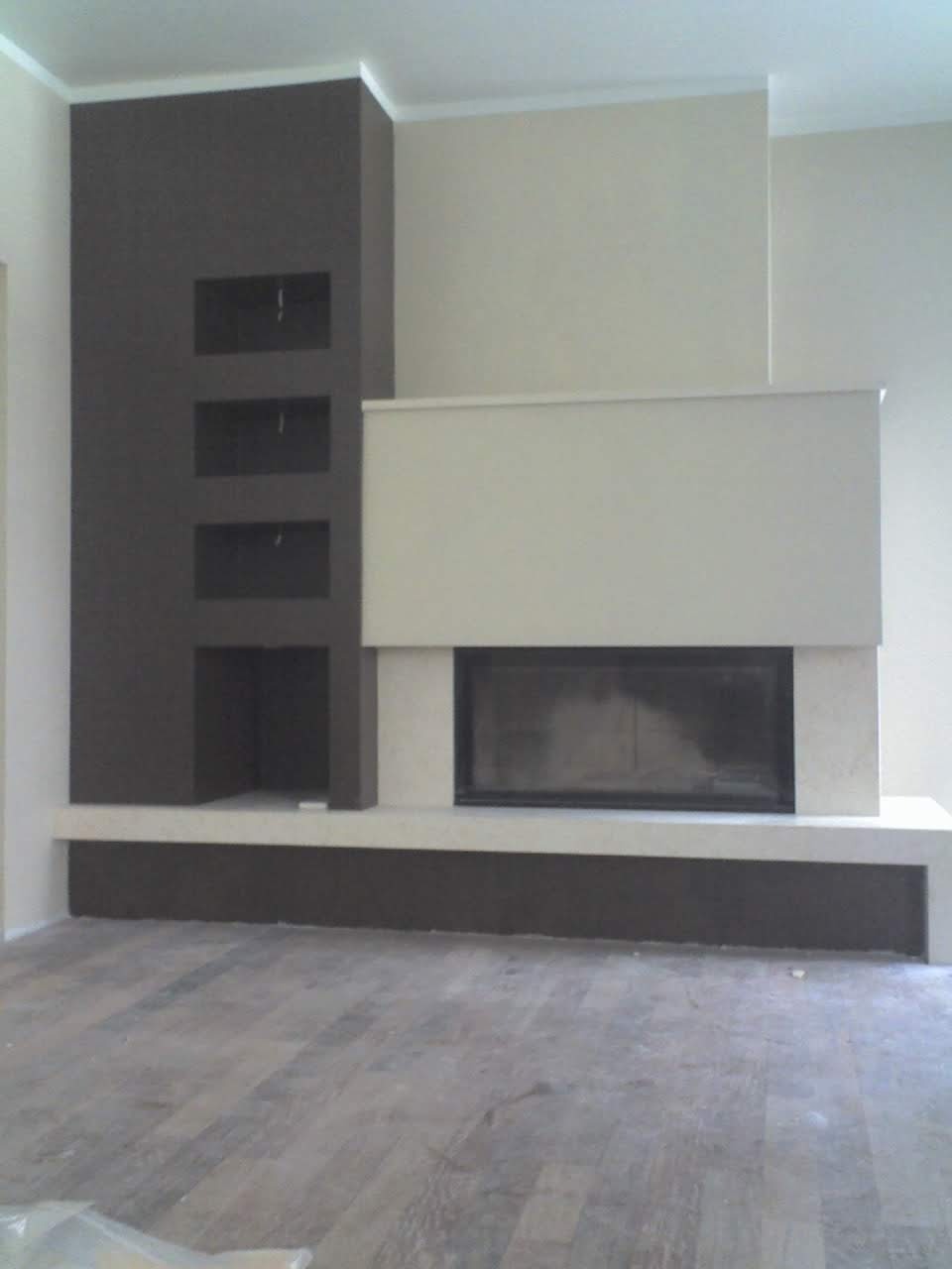 Nowoczesny kominek z ciemnobrązową obudową i wnękami na drewno, wykończony jasnym kamieniem, na tle jasnych ścian i drewnopodobnej podłogi.