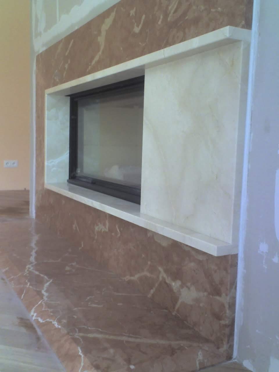 Marmurowa obudowa kominka z czarnym wkładem, widok z boku, ściany w trakcie wykończenia.