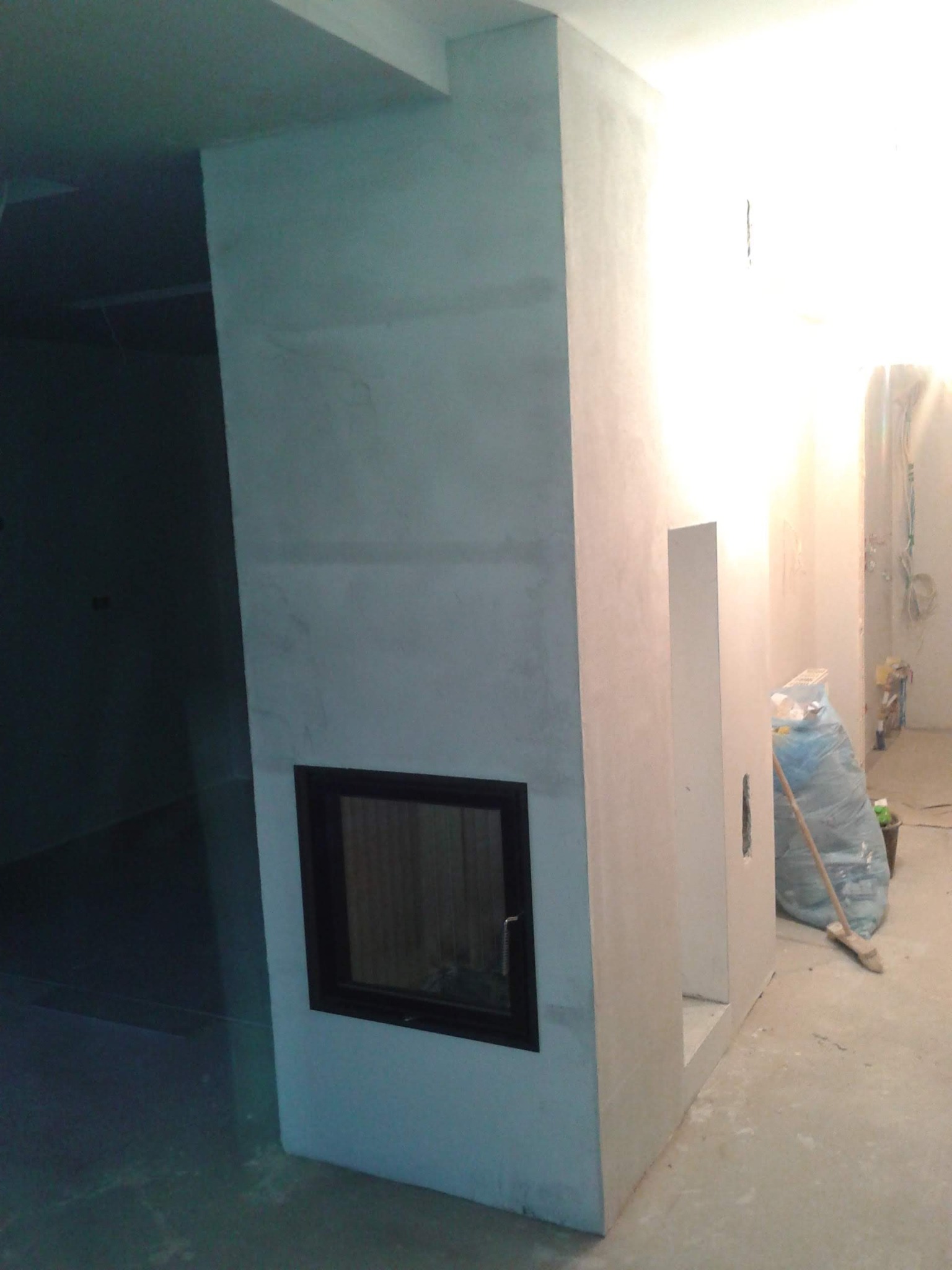 Surowy kominek z czarną wkładką, w trakcie budowy lub wykończenia, z workiem materiałów budowlanych w tle