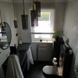 Nowoczesna łazienka z czarną armaturą, wiszącymi lampami z metalową siatką, marmurową podłogą z złotymi żyłami i szarą ścianą z efektem betonu