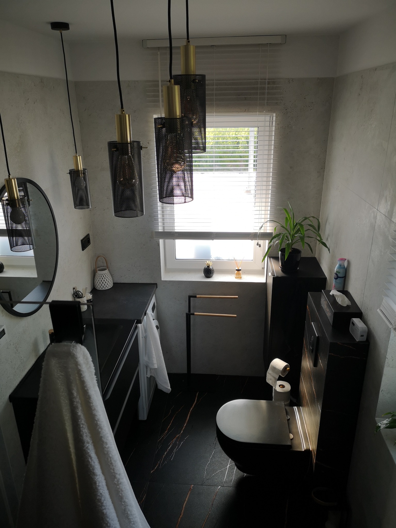 Nowoczesna łazienka z czarną armaturą, wiszącymi lampami z metalową siatką, marmurową podłogą z złotymi żyłami i szarą ścianą z efektem betonu
