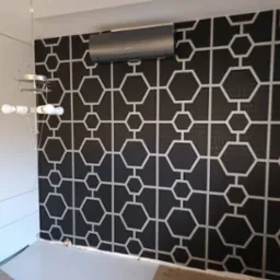 Czarna tapeta w białe geometryczne wzory heksagonów i linii, klimatyzator na ścianie, nowoczesna lampa wisząca i białe meble w tle.