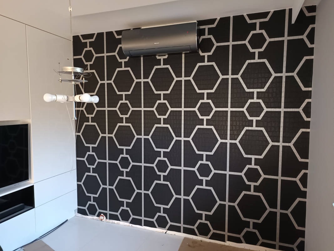 Czarna tapeta w białe geometryczne wzory heksagonów i linii, klimatyzator na ścianie, nowoczesna lampa wisząca i białe meble w tle.