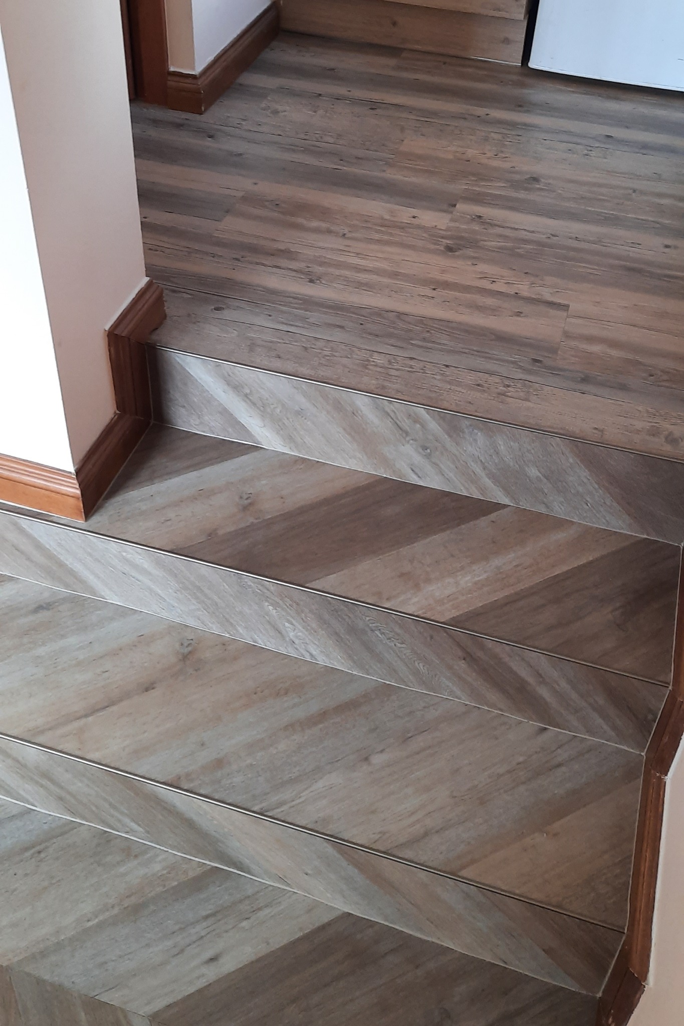 Schody wykończone panelami podłogowymi z wzorem jodełki, z listwami przypodłogowymi w kolorze drewna.