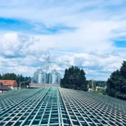 Wykonywanie więźby dachowej na czarnej membranie dachowej, w tle zabudowania gospodarcze i błękitne niebo z chmurami.