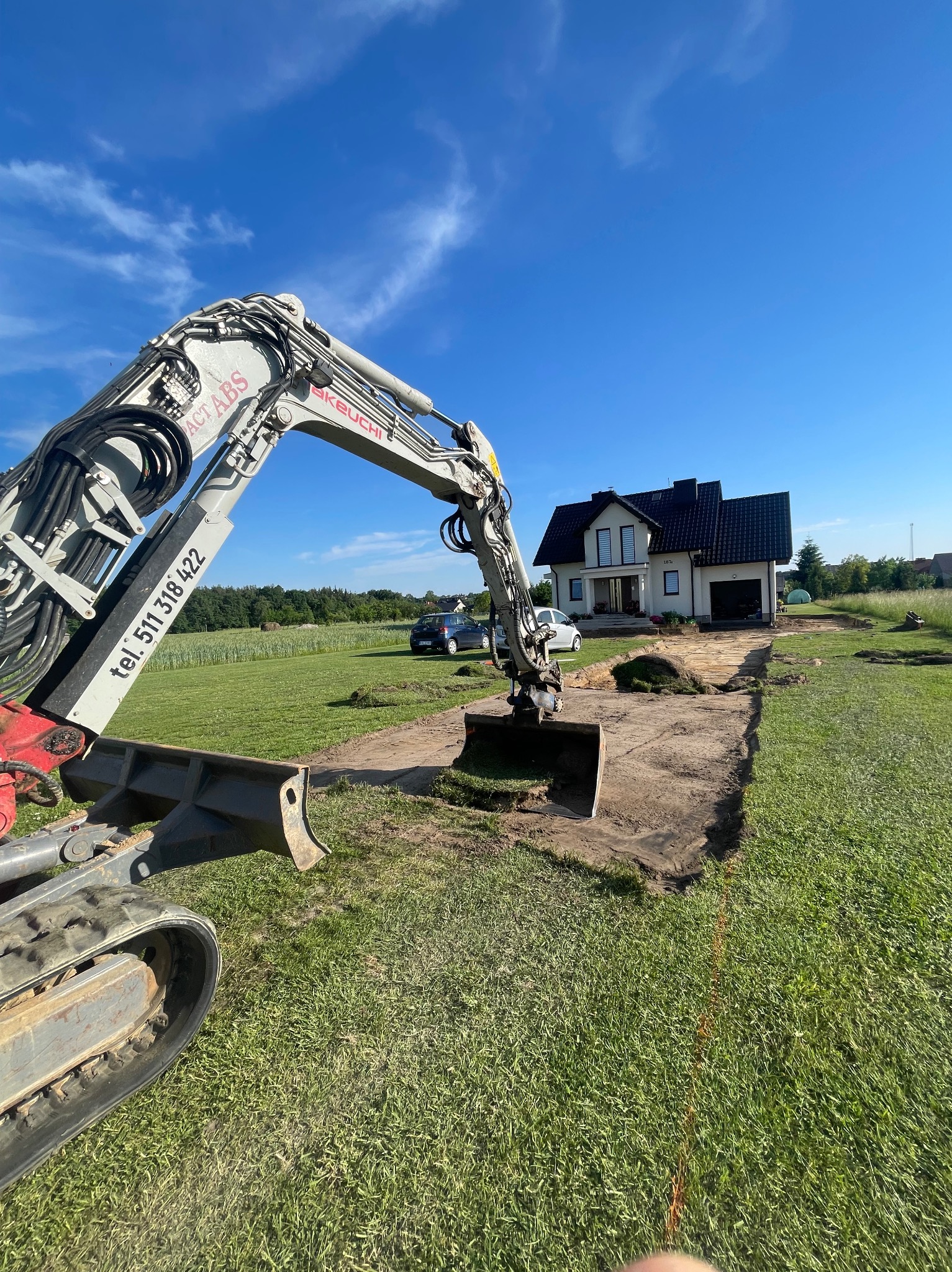 Koparka Takeuchi w Przegini przygotowuje teren pod budowę, widoczny wykopany pas ziemi przed domem.