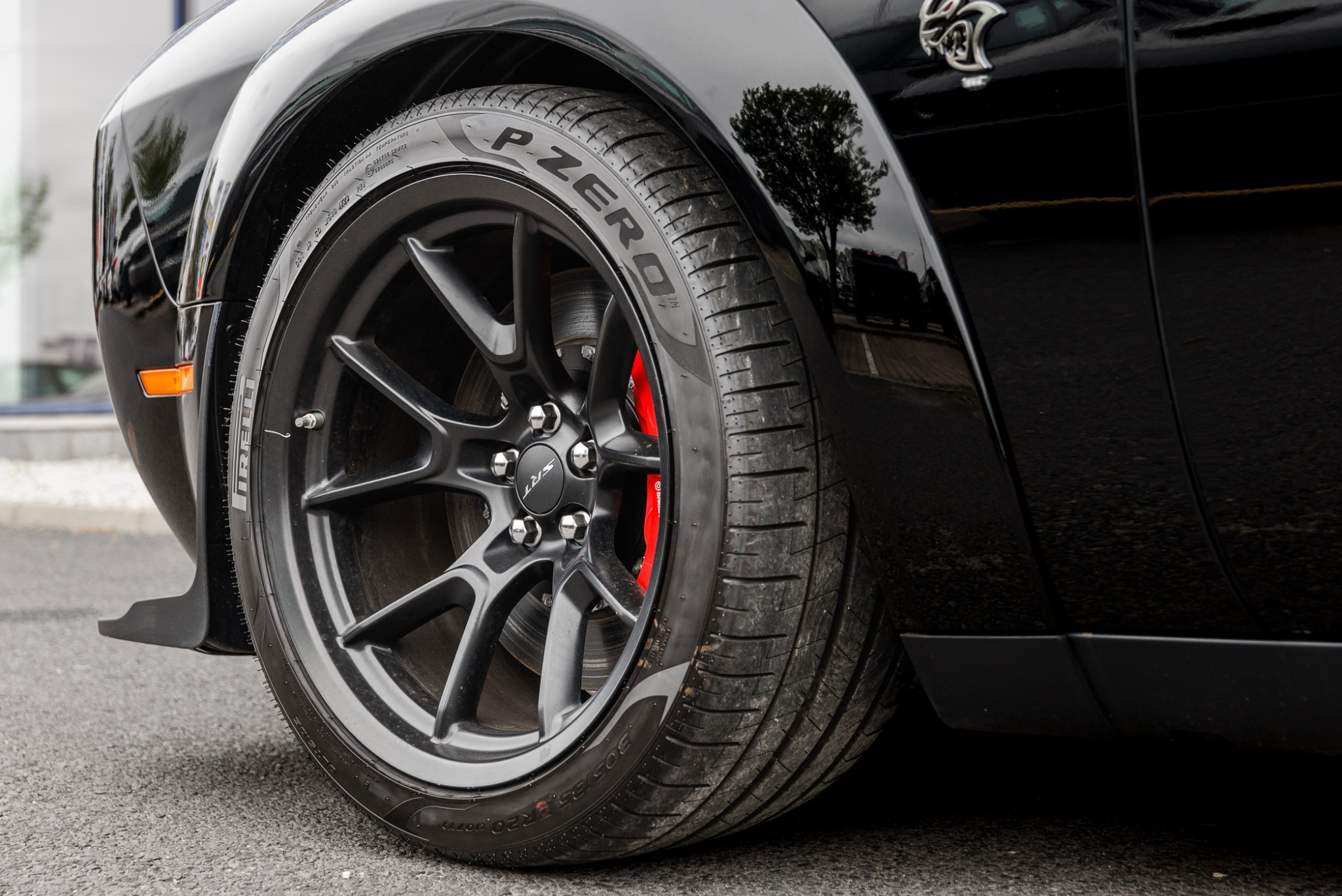 Czarne koło z oponą Pirelli P Zero i czerwonym zaciskiem hamulcowym w samochodzie Dodge Challenger Hellcat, widoczne logo SRT na piaście.