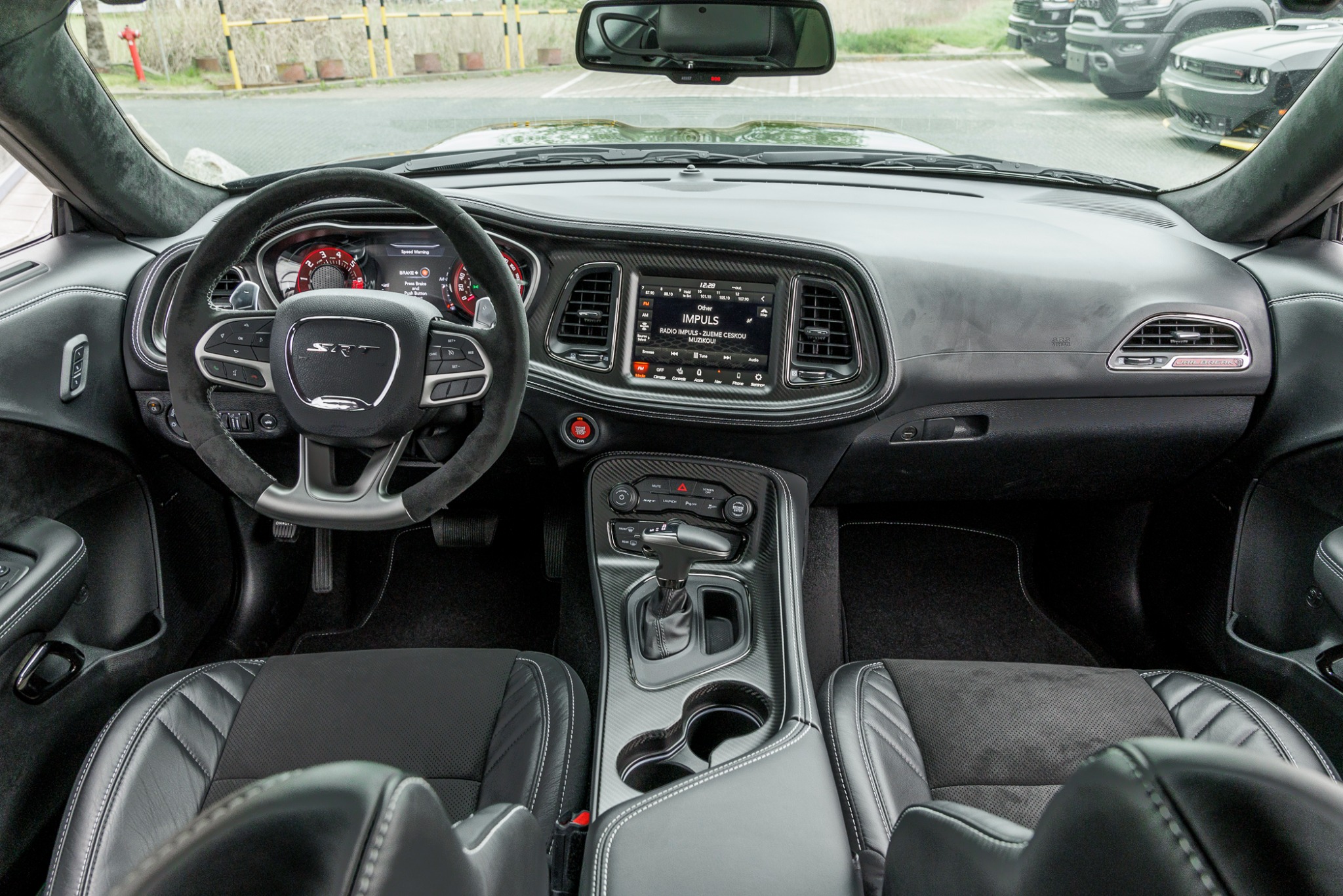 Wnętrze samochodu Dodge Challenger SRT z czarną tapicerką, widok na deskę rozdzielczą, kierownicę z logo SRT, ekran dotykowy z włączonym radiem, fotele z przeszyciami i tunel środkowy z dźwignią...
